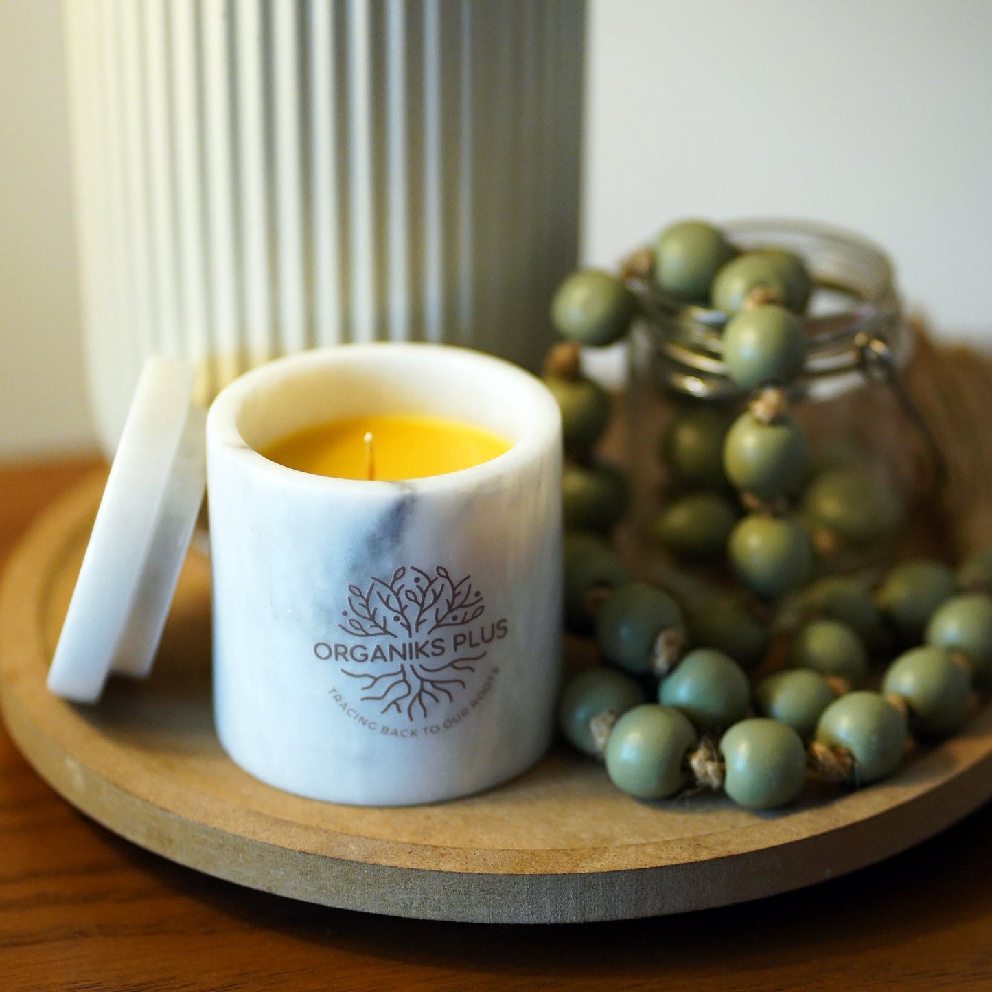 Two candles, one black and one beige, with 'Organiks Plus' branding, placed on a surface with a Chanel magazine in the background.