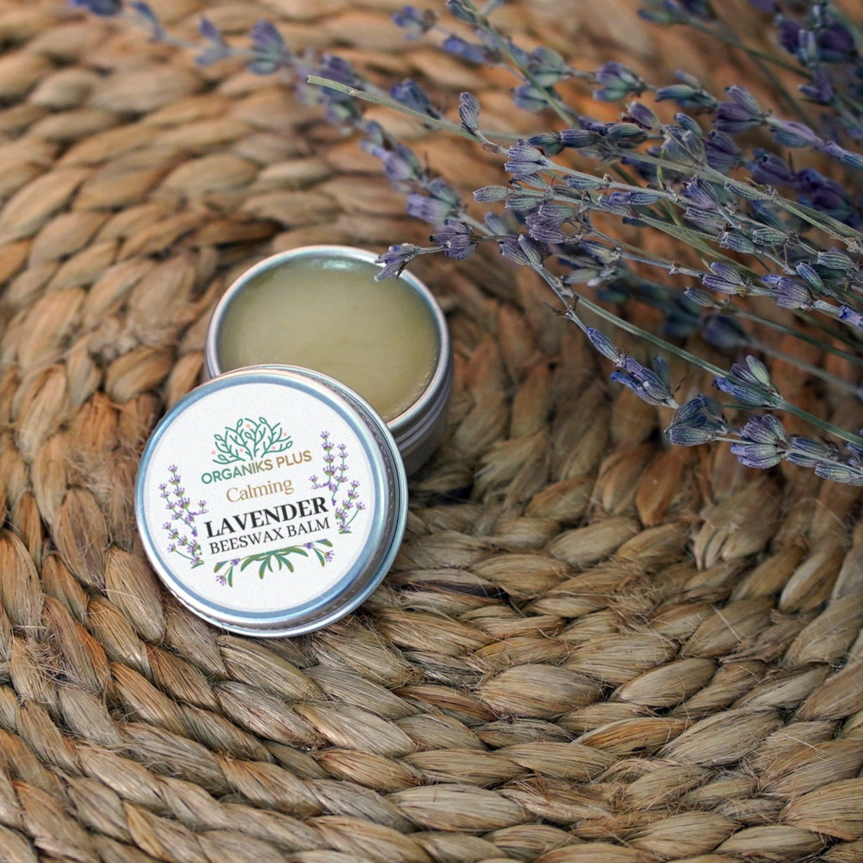 Tin of lavender balm on a woven mat with lavender flowers.