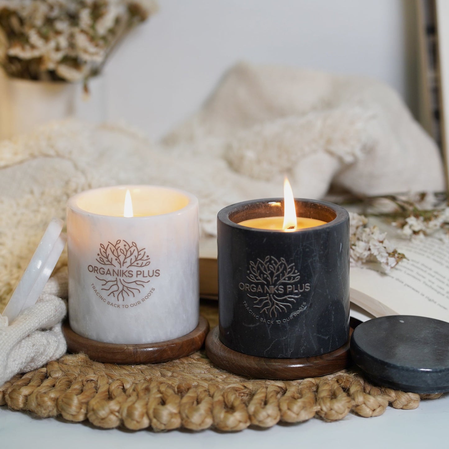 Two lit candles on a textured surface with a book and decorative elements in the background.