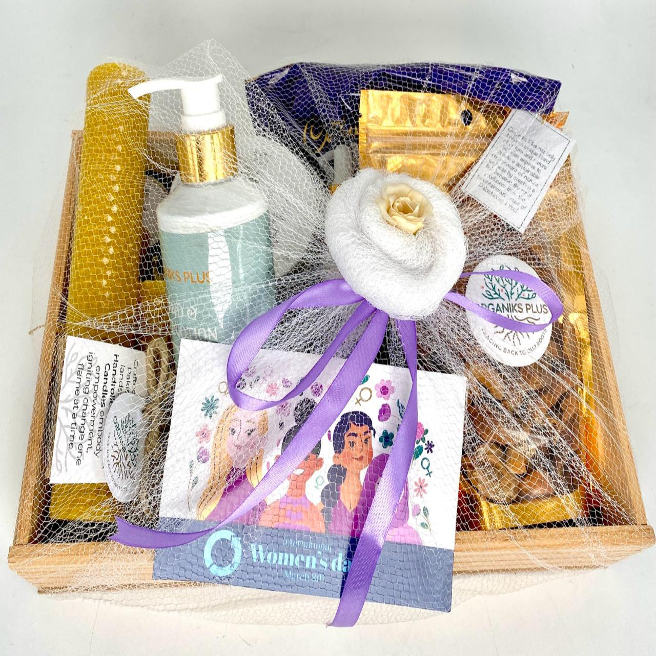 A luxurious self-care gift set arranged on a wooden tray, including a body lotion bottle, beeswax candles, apricot kernels, lip balm, a scented candle, and a face serum pouch, all ribboned and wrapped as a gift.