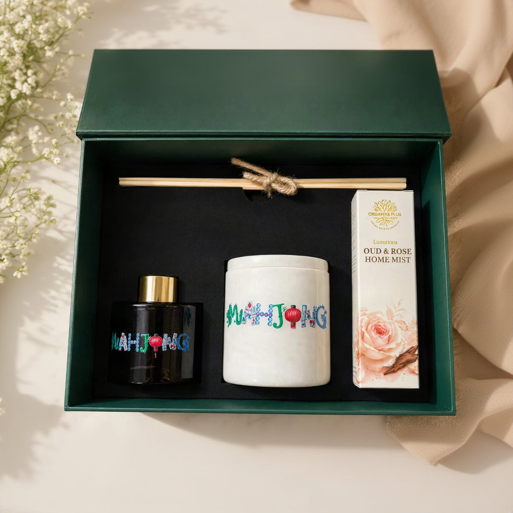 A luxury home fragrance Organiks Plus gift set by NAHTONG, presented in a dark green box. The set includes a black diffuser bottle with a gold cap and colorful logo, a white ceramic jar with colorful lettering, and a white box of Oud & Rose Home Mist with a pink rose illustration.