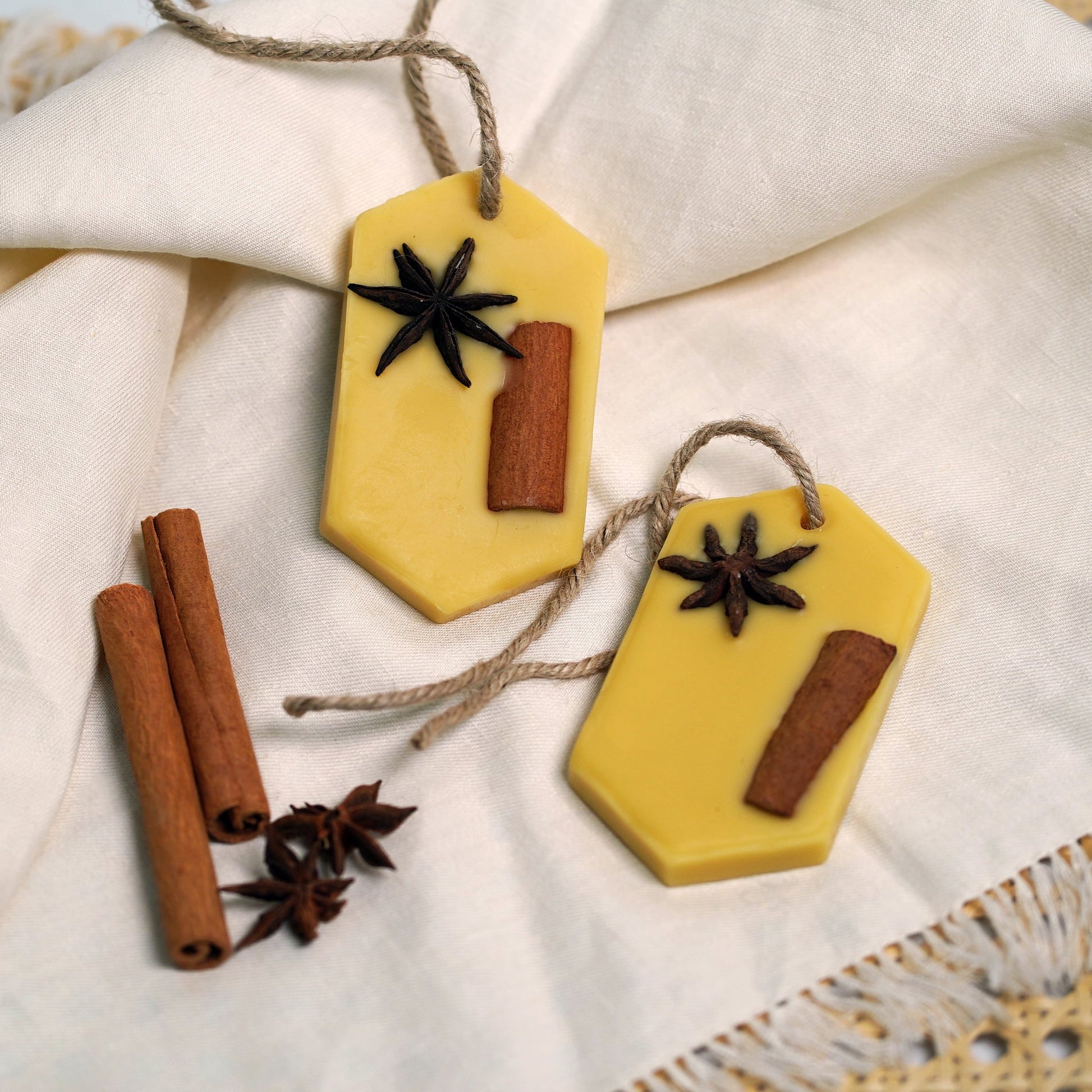 Two yellow hexagonal Beeswax Scented tablets with star anise and cinnamon sticks on a white fabric background.
