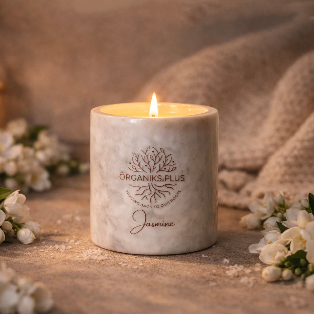 Marble-textured candle with 'The Organiks Plus' logo and 'Jasmine' text, surrounded by white flowers on a wooden surface.