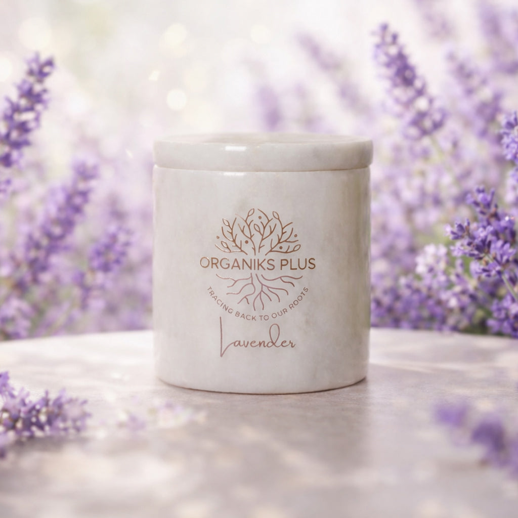 White candle with 'Organiks Plus' branding in front of lavender flowers