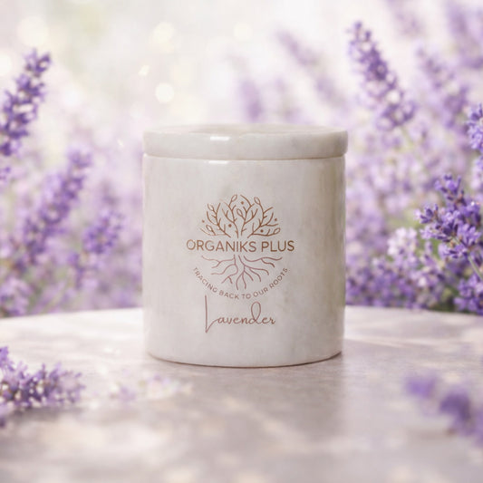 White candle with 'Organiks Plus' branding in front of lavender flowers