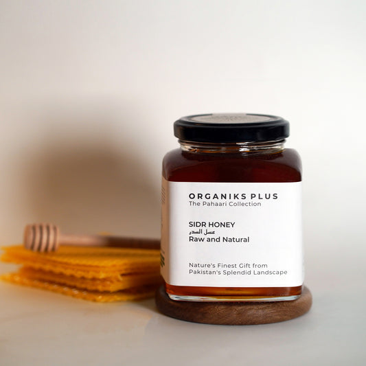 Jar of Organiks Plus Sidr Honey with honeycomb and dipper on a light background